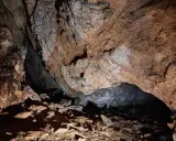 Wnętrze jaskini mylnej, z kamienistym dnem i skalnymi ścianami o rdzawym zabarwieniu, tworzącymi naturalne sklepienie.