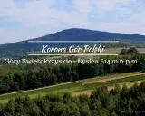 Łysica, najwyższy szczyt Gór Świętokrzyskich, wznosi się dumnie na tle błękitnego nieba. Zielone lasy i pola tworzą malowniczy krajobraz.