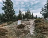 Kamienny słup graniczny i drogowskaz na szczycie góry, otoczone przez świerki. To miejsce, gdzie szlak prowadzi na kowadło szczyt.