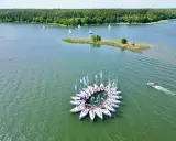 Krąg żaglówek na jeziorze, jakby z lotu ptaka z wieży widokowej na Mazurach. W tle las i mała wyspa.