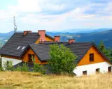 Wielka racza na dachu domu w górach, otoczona zielenią i widokiem na pasma górskie.