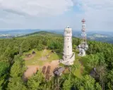 Widok na wieżę widokową i maszt telekomunikacyjny na szczycie góry otoczonej lasem. Jak wielka sowa, wieża obserwuje okolicę.