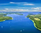 Malownicze mazury widoki: błękitne jezioro, zielone wyspy i żaglówki pod błękitnym niebem.