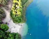 Plaża nad jeziorem tętni życiem. Ludzie odpoczywają na piasku, kąpią się w krystalicznie czystej wodzie, ciesząc się letnim dniem.