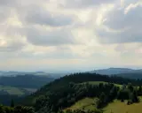 Malownicze **góry Sowie** oferują liczne **atrakcje** turystyczne. Widok na zielone wzgórza i lasy pod zachmurzonym niebem.