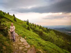Kobieta na kamiennym szlaku na Śnieżkę, otoczona zielonymi zboczami i drzewami.