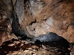Wnętrze jaskini mylnej, z kamienistym dnem i skalnymi ścianami o rdzawym zabarwieniu, tworzącymi naturalne sklepienie.
