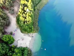 Plaża nad jeziorem tętni życiem. Ludzie odpoczywają na piasku, kąpią się w krystalicznie czystej wodzie, ciesząc się letnim dniem.