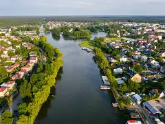 Malowniczy widok na Augustów i jego atrakcje: rzeka, zielone brzegi, domy i las w tle.
