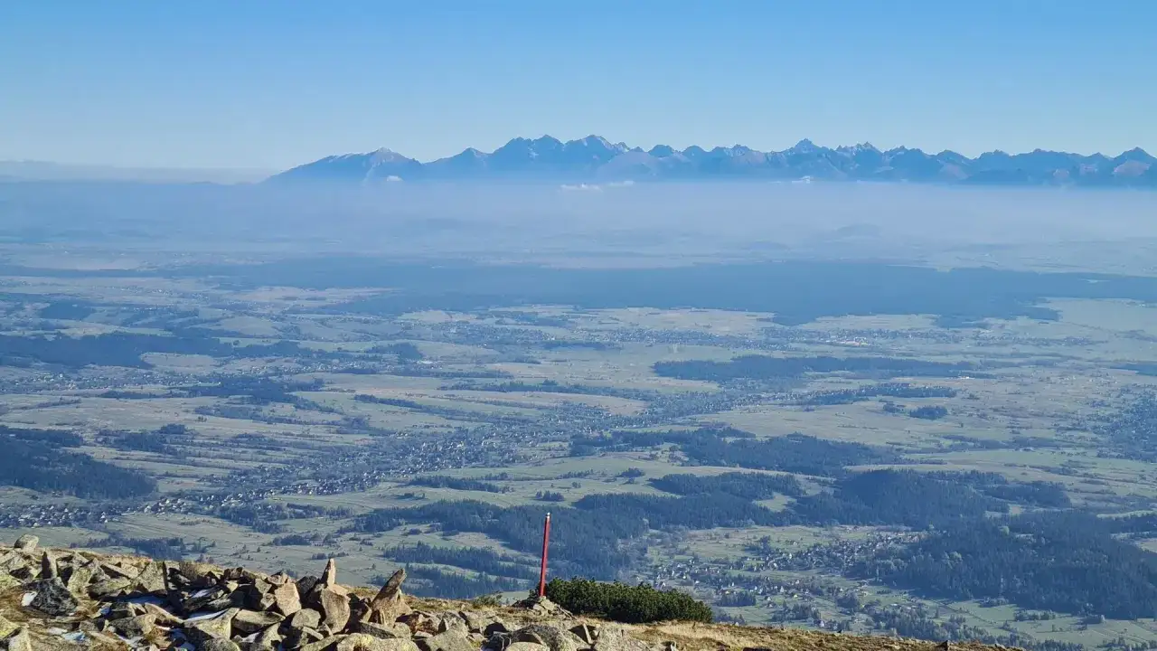 Widok z Babiej Góry na Tatry w oddali, spowite mgłą. Na pierwszym planie kamieniste zbocze.