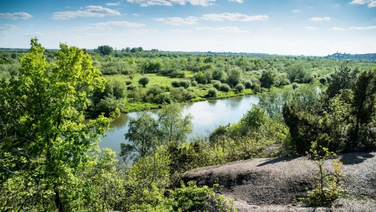 Krajobraz z rzeką i bujną zielenią. W oddali widać miasteczko, jakby wyłaniające się zza gór pieprzowych.