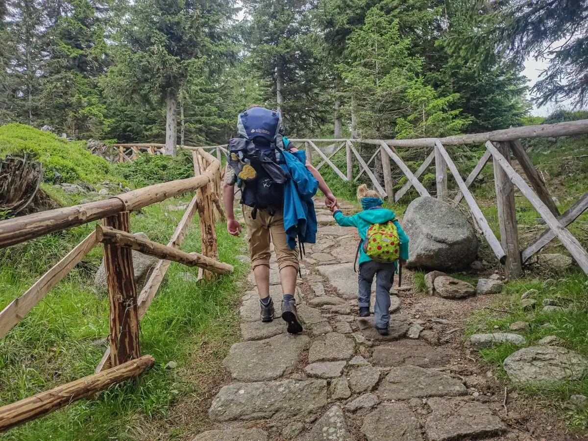 Dzieci i dorośli wędrują kamienistym szlakiem w Karkonoszach, otoczeni lasem. To piękna pielgrzymka w Karpaczu.