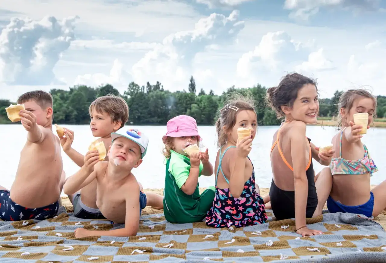 Dzieci jedzą lody na plaży nad jeziorem. Słońce, woda i słodkości tworzą idealny letni dzień.