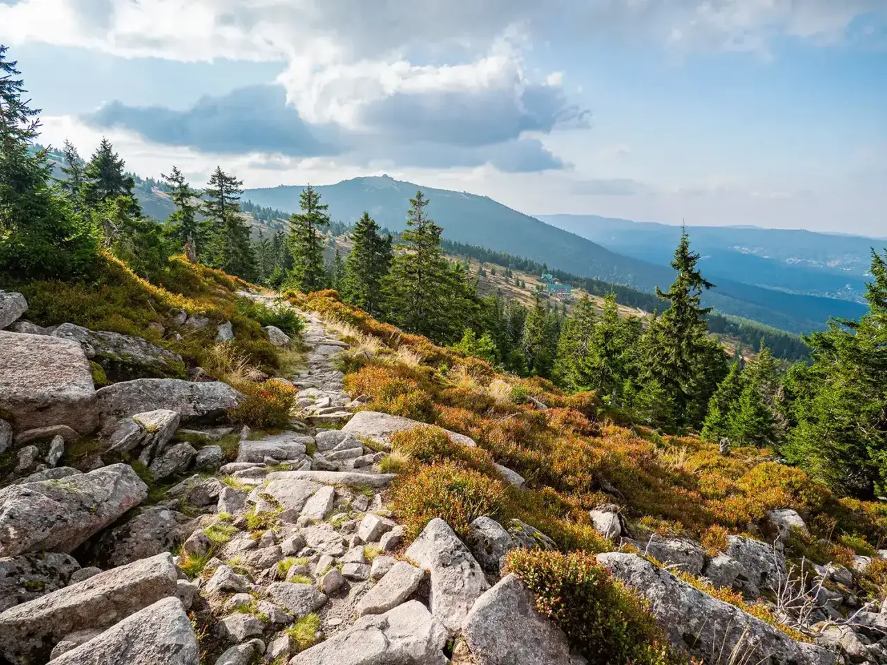 Kamienista ścieżka prowadzi przez skalisty teren, przypominający naturalny skalny stół, w kierunku górskich szczytów.