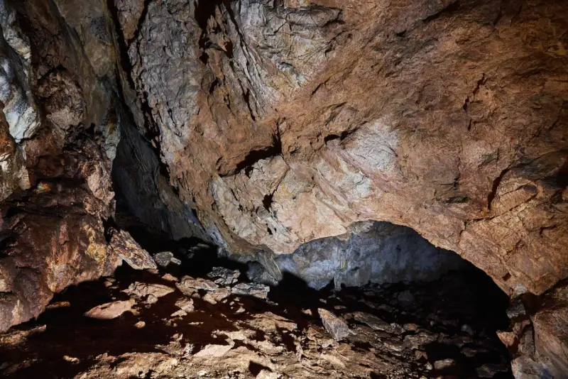 Wnętrze jaskini mylnej, z kamienistym dnem i skalnymi ścianami o rdzawym zabarwieniu, tworzącymi naturalne sklepienie.