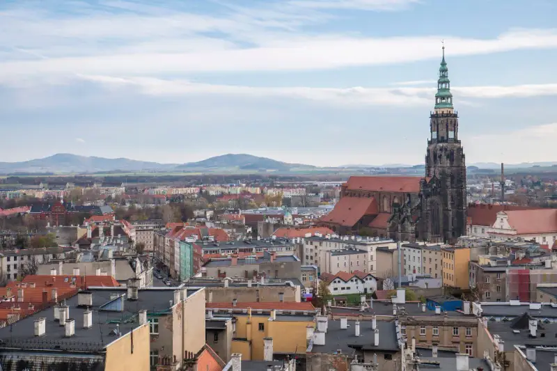 Widok na miasto z dominującą wieżą katedry. W oddali góry. Odkryj **Świdnica atrakcje**!
